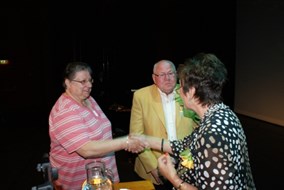 De burgemeester feliciteert Mevouw van de Pol, Cor met lintje kijkt toe